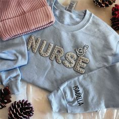 two sweaters with the word nurse on them next to pine cones and christmas decorations