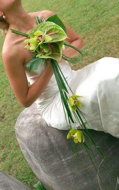 a woman in a wedding dress sitting on a rock with flowers and greenery around her neck