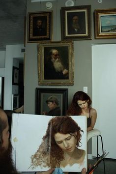 a woman holding up a book with pictures on the wall behind her and people looking at it