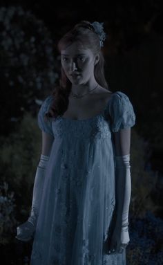 a woman in a blue dress and white gloves standing in the dark with her hands on her hips