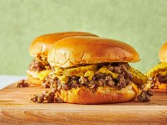 two sloppy joes sitting on top of a wooden cutting board next to each other