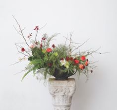 a vase filled with lots of flowers on top of a white table next to a wall