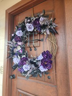 a wreath with purple flowers hanging on the front door to a house that has a wooden door