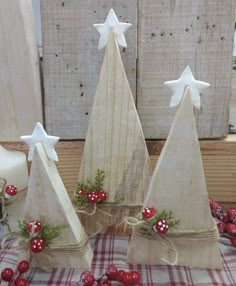 three small christmas trees with white stars on top and berries around the base, sitting on a plaid tablecloth