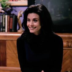 a woman sitting in front of a wooden table with a bookcase on the side