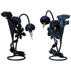 two black metal vases with flowers and leaves on them, one has a bird's beak sticking out of it