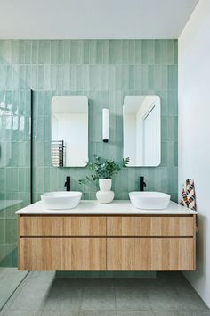 two white sinks sitting on top of a wooden cabinet next to a green tiled wall