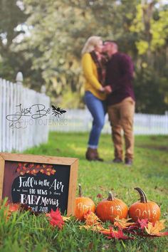 a couple kissing in the grass with pumpkins and chalkboard sign next to them