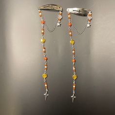 two orange and yellow beads are attached to silver hair clips on a gray surface with a pair of scissors