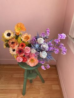 an arrangement of colorful flowers in a green vase on a small table next to a pink wall