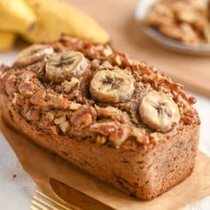 a loaf of banana nut bread sitting on top of a wooden cutting board next to bananas