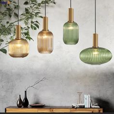 three green glass pendant lights hanging from the ceiling above a table with books and vases on it