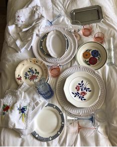 a table topped with lots of white plates and dishes on top of a bed covered in blankets