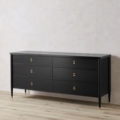 a black dresser with gold handles and drawers on it's sides, against a white wall