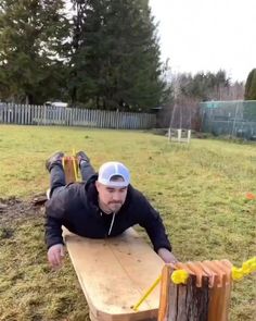 a man laying on top of a wooden bench next to a tree stump in a field