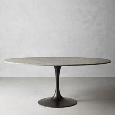 an oval marble table with black metal base and round top, against a white wall