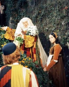 two women dressed in medieval clothing standing next to each other near a wall with ivy growing on it