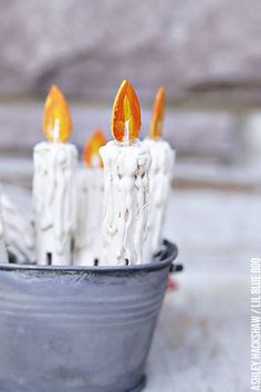 some candles are sitting in a bucket on the table and one candle is turned orange