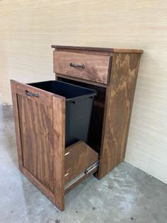 a wooden cabinet with two drawers and a black trash can in the bottom right corner