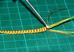 a pair of scissors is hooked up to a piece of yellow and orange thread on a green surface