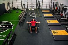 a man sitting in a gym with his arms wide open, surrounded by rows of exercise equipment