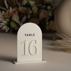 a white table number sitting on top of a table next to a bouquet of flowers