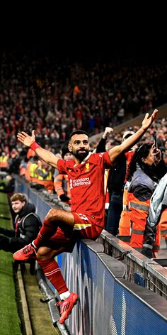 a soccer player is sitting on the edge of a wall with his arms in the air