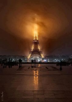 the eiffel tower lit up at night with people standing in front of it