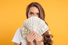 a woman covering her mouth with money in front of her face on an orange background