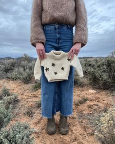 a woman holding a sweater in the desert with her hands on her hips and wearing boots