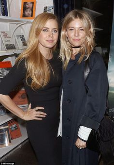 two women standing next to each other in front of a book shelf with books on it