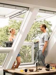 a man and woman standing in an open room with windows looking out onto the trees