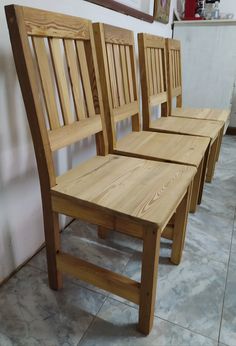 three wooden chairs sitting next to each other in a room with tile flooring and white walls