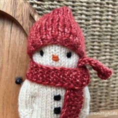 a knitted snowman ornament hanging from a wooden door with a red scarf around it