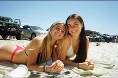 two young women laying on the beach in front of their cars and smiling at the camera