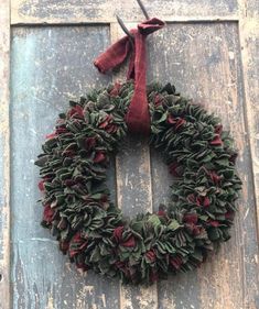 a wreath hanging on the side of a wooden door with a red ribbon around it