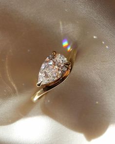 a diamond ring sitting on top of a white satin covered surface with sunlight shining through it