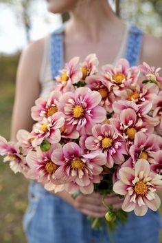 a woman in overalls holding a bouquet of pink flowers