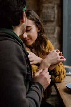 a man and woman sitting at a wooden table with their hands on each other's chest