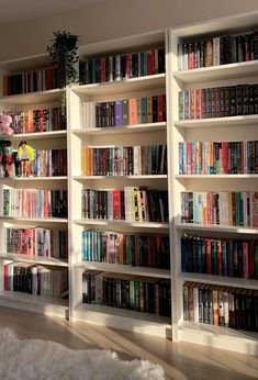 a room filled with lots of books on top of white bookcases next to a window