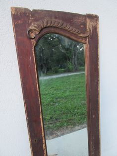 an old mirror sitting on the side of a wall next to a grass covered field