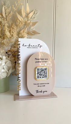 a white vase with flowers and a qr code on it next to a card