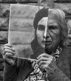 an old woman holding up a black and white photo with the image of a woman's face on it