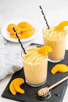 two glasses filled with orange smoothie on top of a black slate tray next to sliced peaches