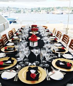 the table is set with black linens, gold plates and red roses on them