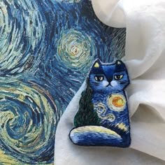 a blue cat sitting on top of a piece of cloth next to a painting with stars