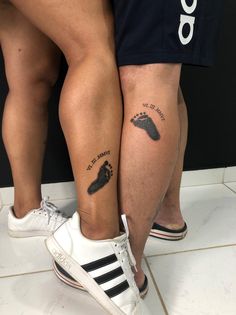 two people standing next to each other with tattoos on their legs and foot prints on them