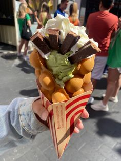 a person holding up an ice cream cone with chocolate, oranges and whipped cream