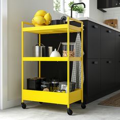 a yellow cart is in the middle of a kitchen with black cabinets and countertops