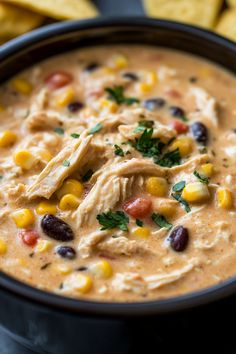 a black bowl filled with chicken and corn soup surrounded by tortilla chips on the side